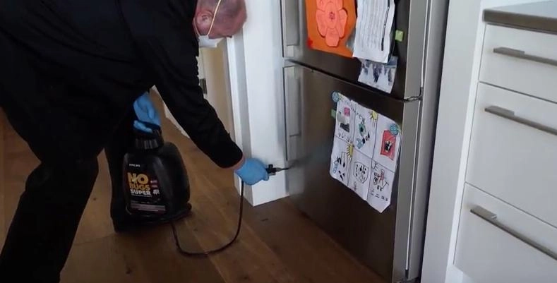 Technician treating behind a refrigerator for house mice